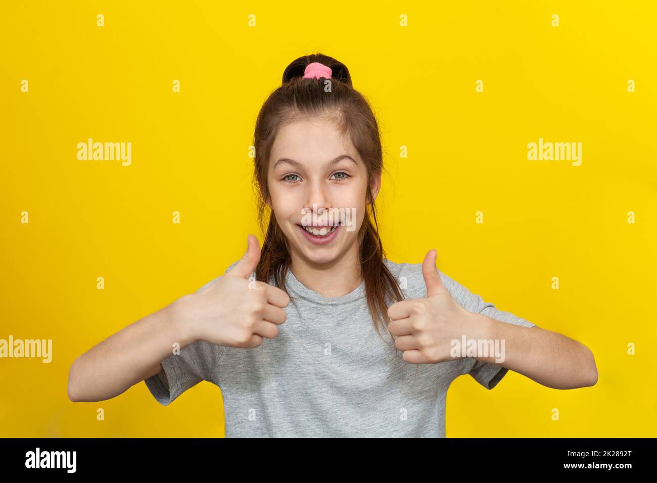 Photo portrait petite fille souriant montrant le pouce vers le haut mouvement isolé couleur jaune vif arrière-plan Banque D'Images