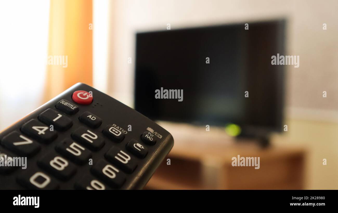 Main tenant une télécommande de télévision et des programmes de surf sur la télévision. Regardez, allumez ou éteignez le téléviseur dans le salon ou la chambre sur la table de nuit à écran noir. Copier l'espace. Banque D'Images