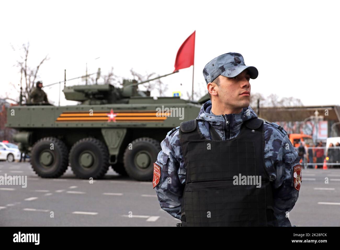 Soldat des forces militaires russes de la Garde nationale dans un gilet à l'épreuve des balles sur fond de véhicule blindé dans la rue de la ville Banque D'Images