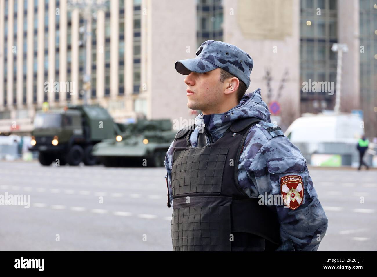 Soldat des forces militaires russes de la Garde nationale dans un gilet à l'épreuve des balles sur fond de véhicule blindé dans la rue de la ville Banque D'Images