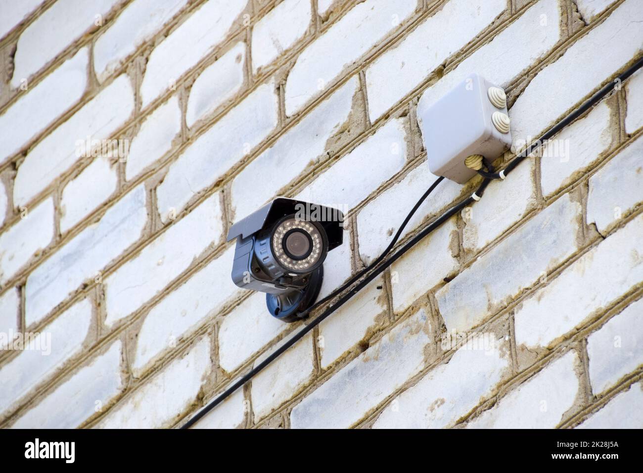 Caméra vidéo à l'allumage est accroché au mur. Mur de briques blanches et d'une caméra vidéo avec des fils. Banque D'Images