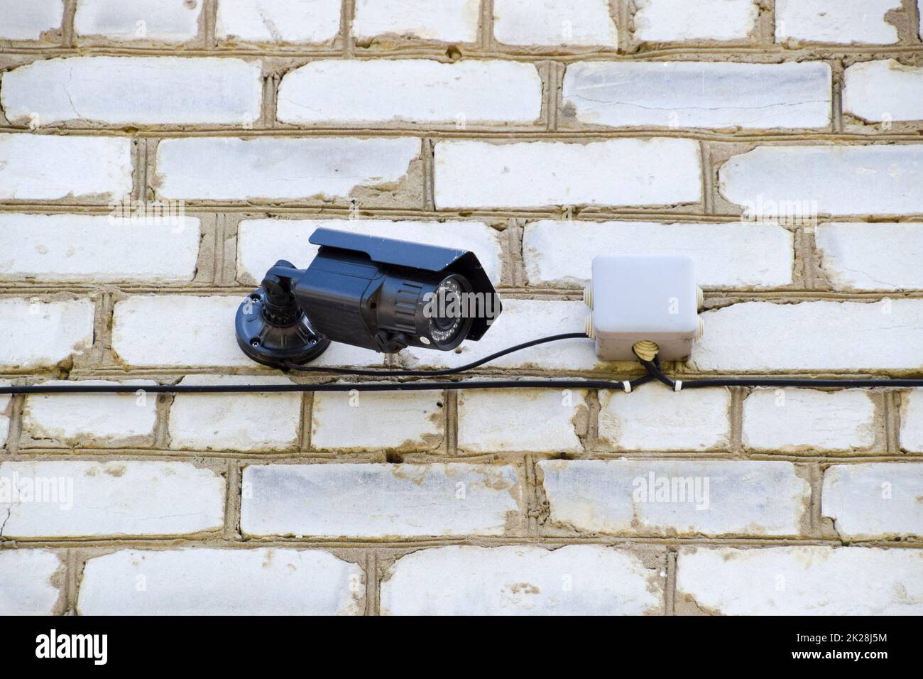 Caméra vidéo à l'allumage est accroché au mur. Mur de briques blanches et d'une caméra vidéo avec des fils. Banque D'Images