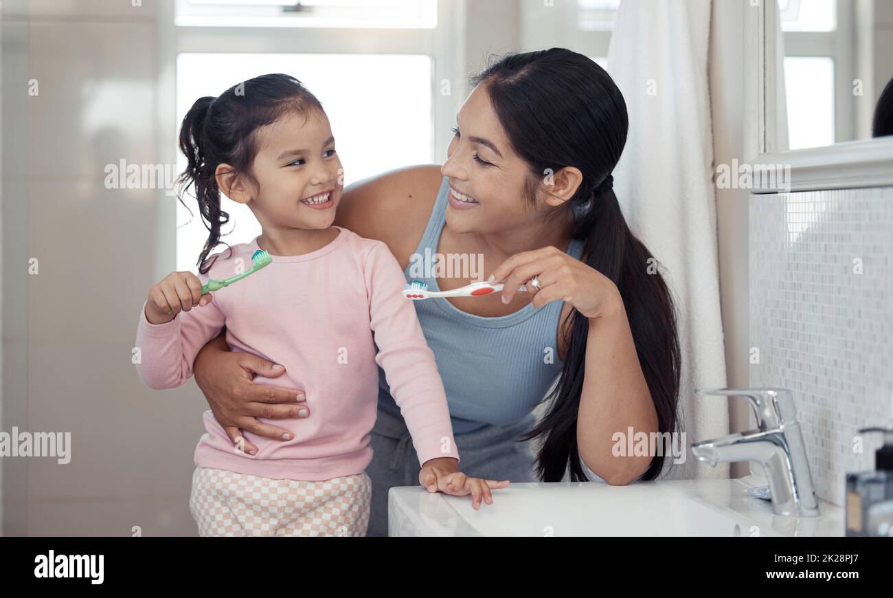 Mère avec fille apprenant à brosser les dents avec brosse à dents ensemble dans la salle de bains pour le bien-être oral ou dentaire. Heureux, amour et soins maman enseignant enfant ou Banque D'Images