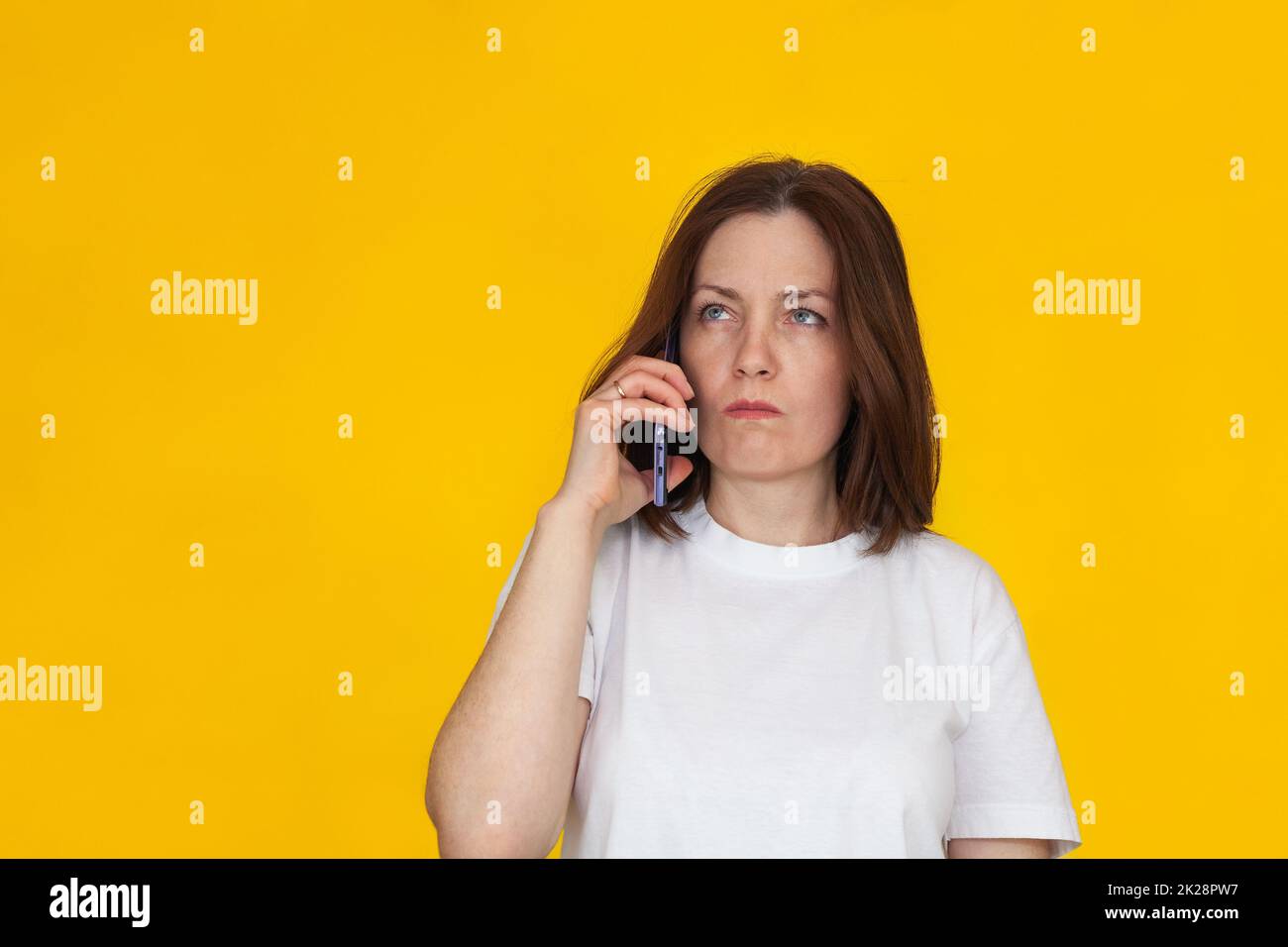 Portrait d'une femme brunette européenne souriante portant un T-shirt blanc sur fond jaune parlant sur un téléphone portable. Banque D'Images