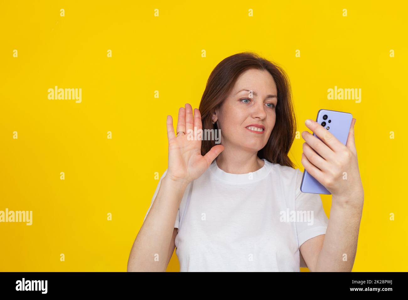 Portrait d'une femme brunette européenne souriante portant un T-shirt blanc sur fond jaune parlant sur un téléphone portable. Banque D'Images