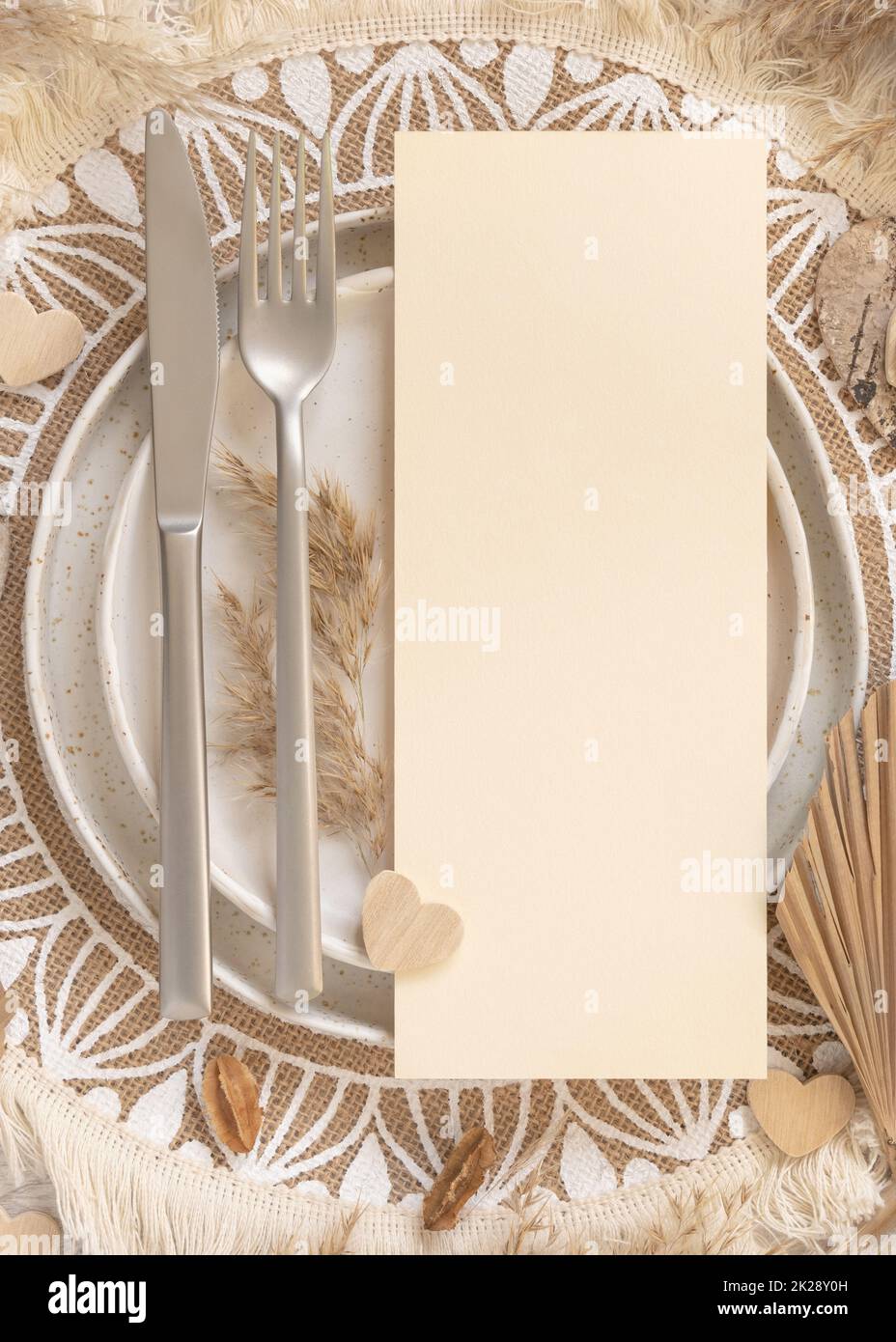 Table de boho place avec carte blanche verticale sur l'assiette près des coeurs et des fleurs séchées Banque D'Images