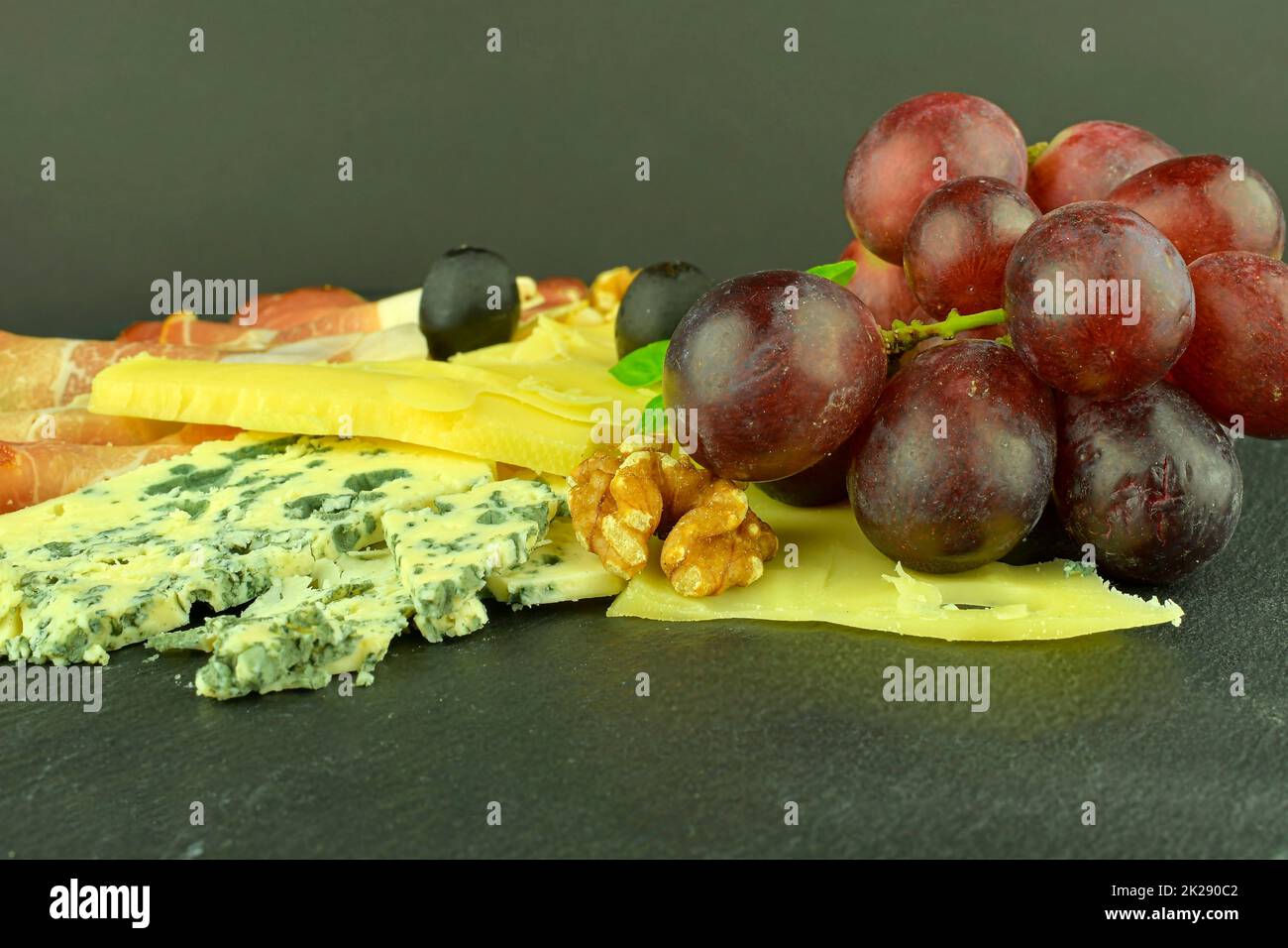 Plateau avec jambon Schwarzwald, fromages, noix, olives noires.Décoration au basilic.Nourriture sur fond d'ardoise.Copier l'espace Banque D'Images