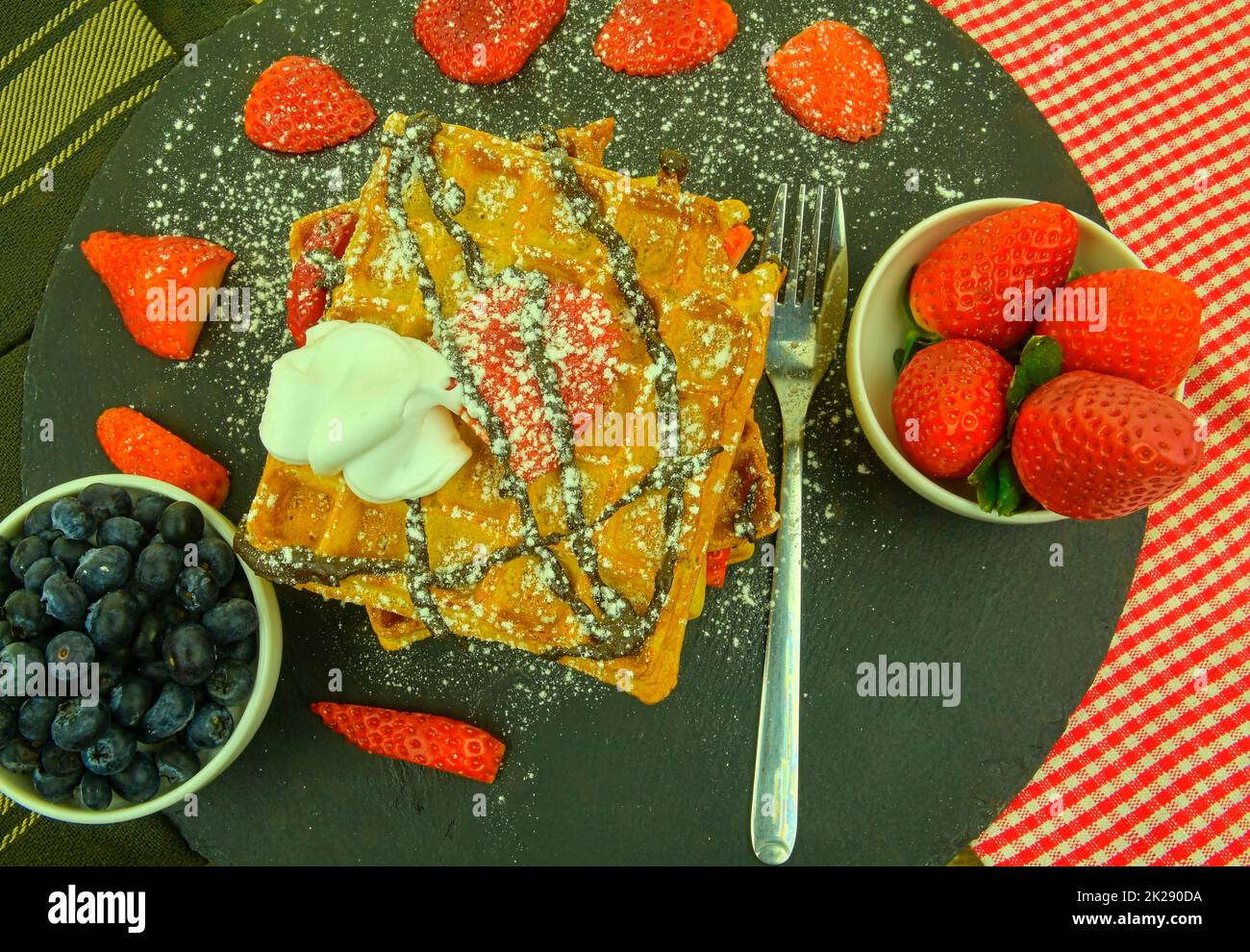 Gaufres belges traditionnelles avec myrtilles et fraises.Chocolat fondu et crème fouettée sur les gaufres.Vue de dessus.Arrière-plan en ardoise noire. Banque D'Images