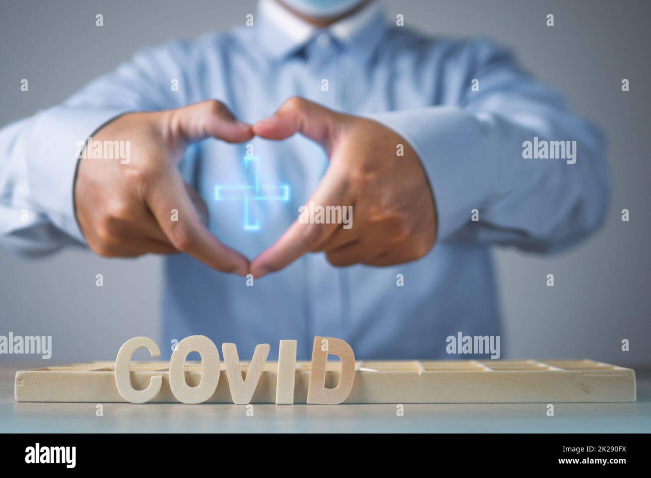 Le courtier présente l'assurance Covid. Forme du cœur avec les mains. Les textes en bois sont sur la table. Gros plan moyen. Banque D'Images