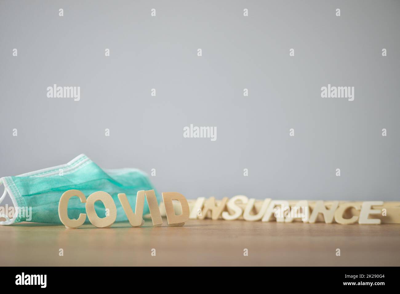 Concept d'assurance Covid. Texte en bois avec masque médical vert. L'objet se trouve sur la table avec de l'espace sur le mur. Ce cliché était centré sur le texte au recto. Banque D'Images