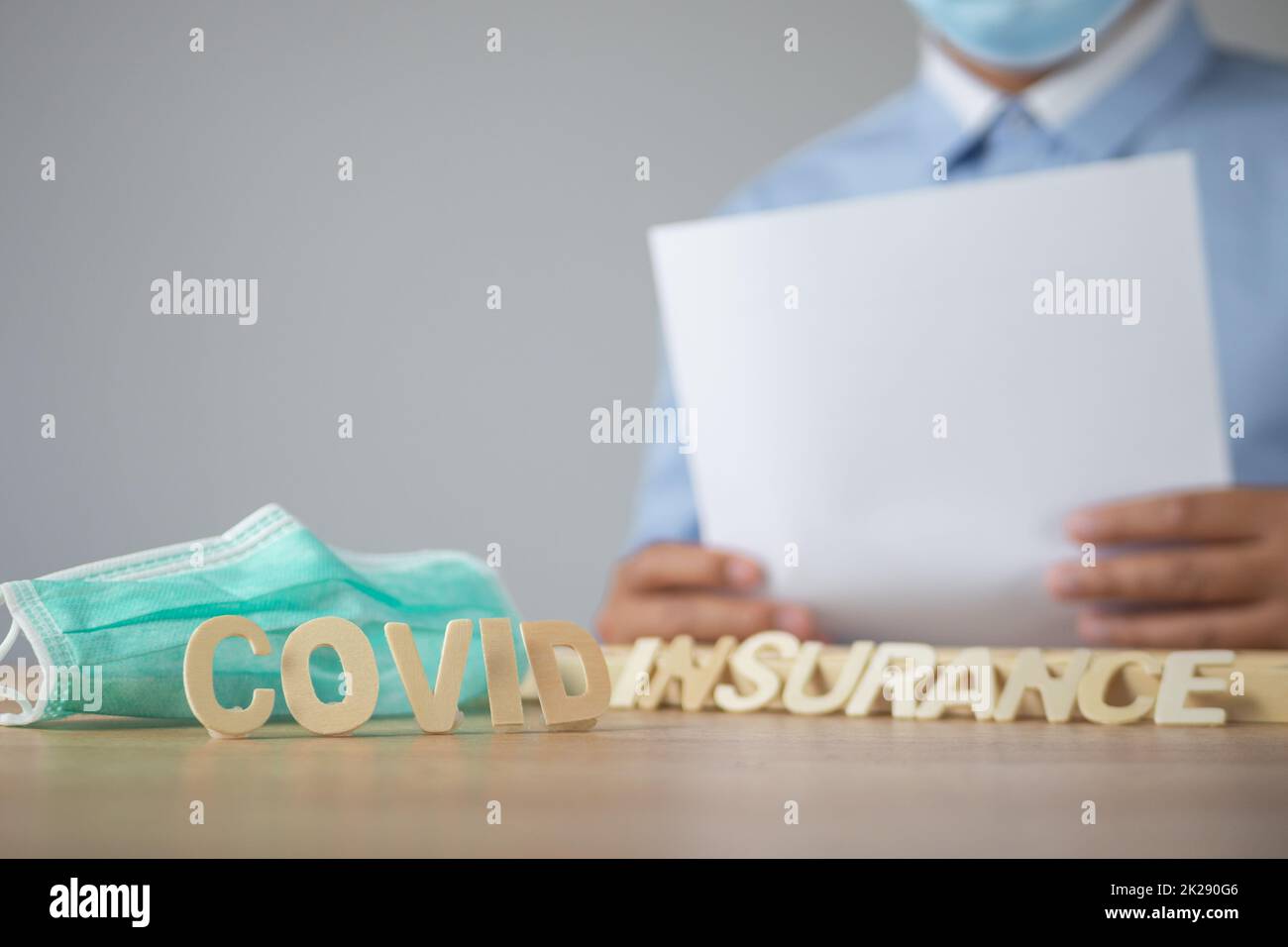 Le courtier présente l'assurance Covid. Texte en bois avec masque médical vert. L'objet se trouve sur la table avec de l'espace sur le mur. Ce cliché était centré sur le texte au recto. Banque D'Images