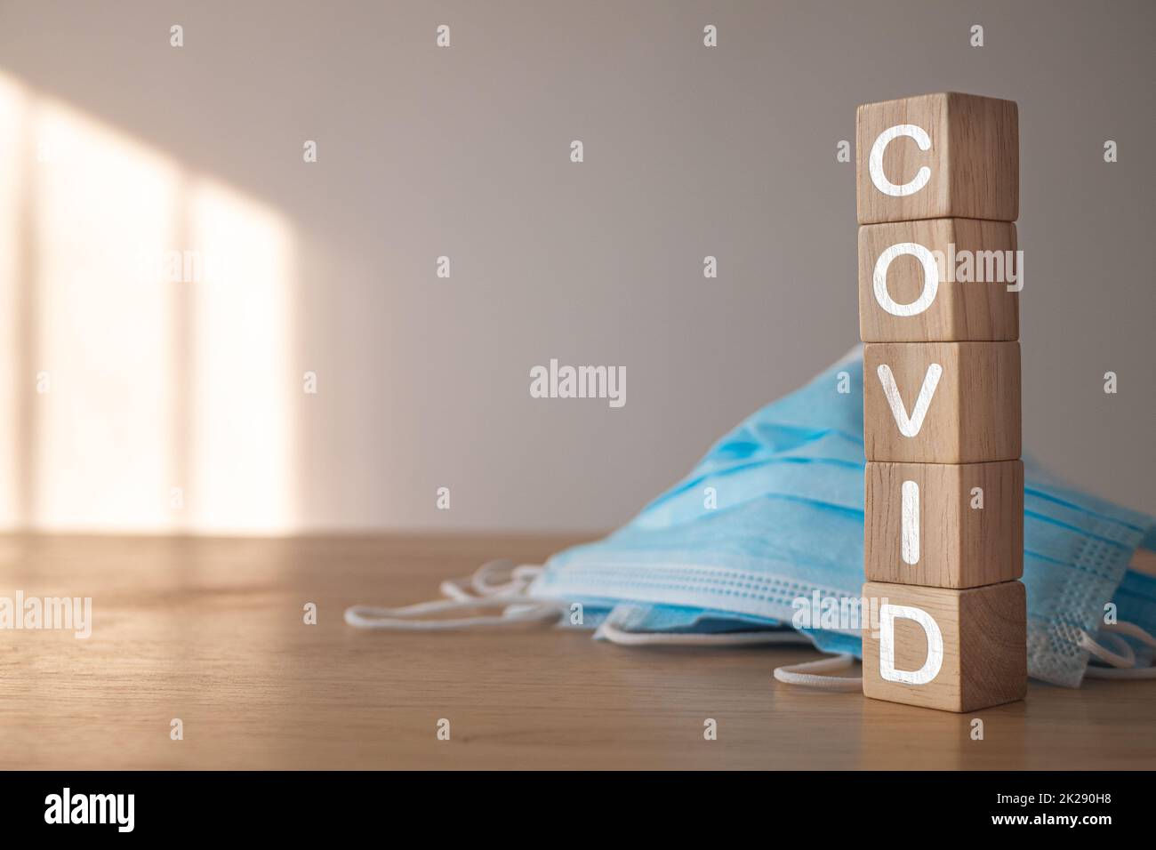 Ce concept montre une campagne pour un port correct du masque. Blocs de bois avec texte, COVID. Masque médical bleu sur la table. Protection contre les maladies telles que la grippe, la grippe, Covid, Dust, PM2,5. Banque D'Images
