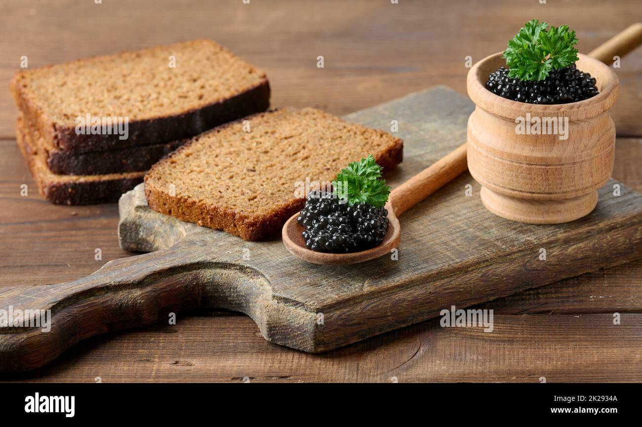 caviar de paddlefish noir granuleux frais en cuillère en bois marron sur une table brune, gros plan Banque D'Images