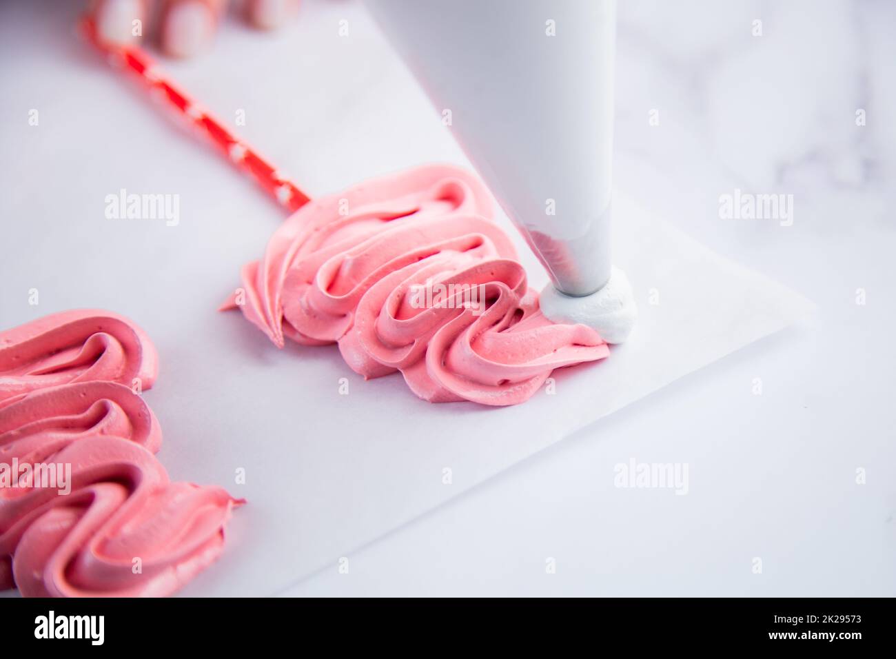 Sur le parchemin léger, il y a des capuchons de meringue rose sur des bâtons, le cuisinier fait un pompon et une frite à partir d'un sac de pâte de meringue blanche. Banque D'Images