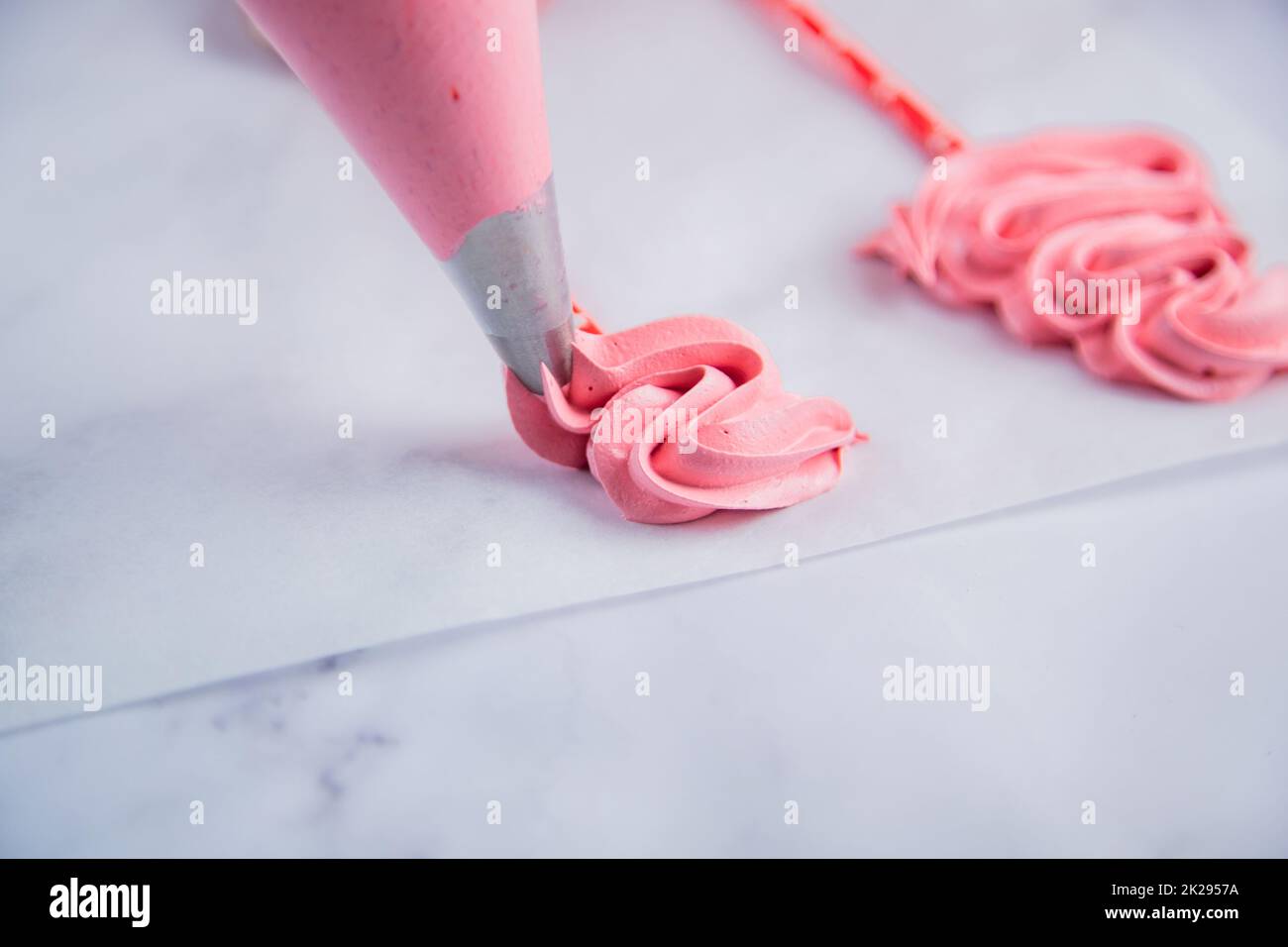 Dans le sac à pâtisserie, un bizet rose est posé sur du papier à pâtisserie avec des boucles sous la forme d'un arbre de Noël. Banque D'Images