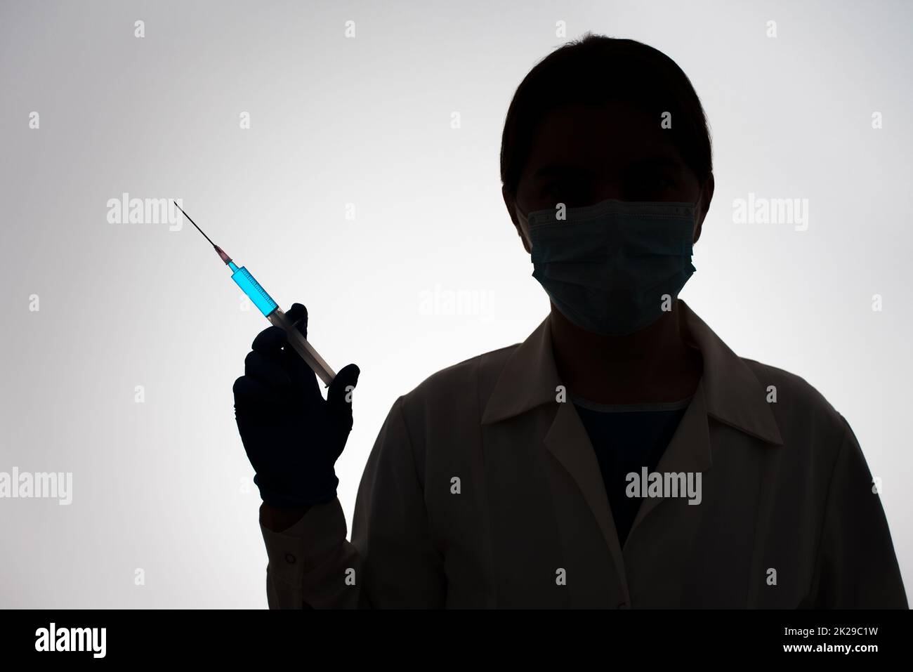 Silhouette d'un médecin avec une seringue remplie de liquide bleu. Concept de vaccination. Banque D'Images