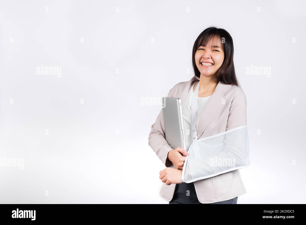 Femme d'affaires asiatique confiante souriante bras cassé après accident et porter une attelle de bras pour le traitement mais elle doit encore travailler elle tient un ordinateur portable Banque D'Images