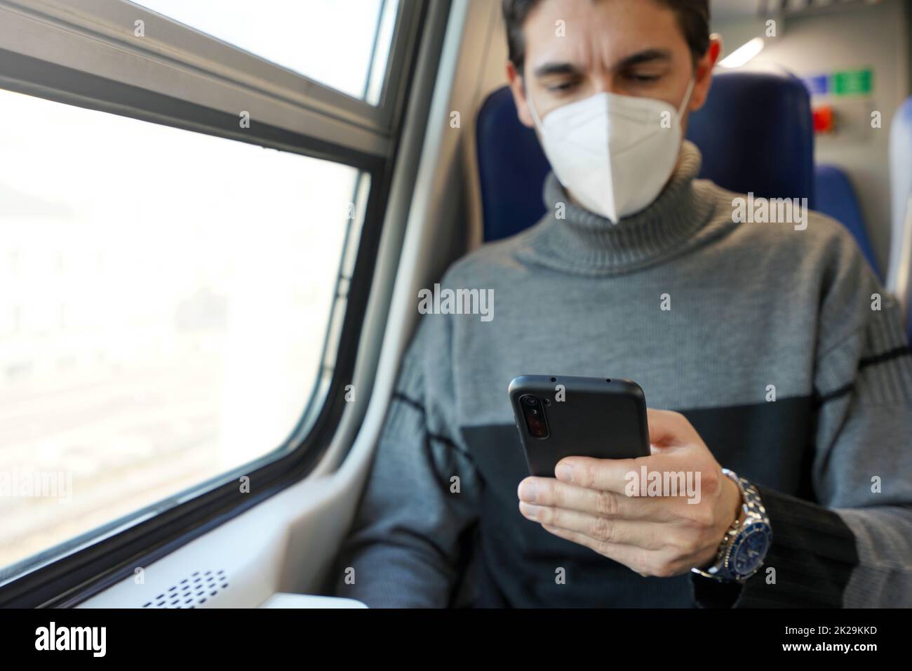 Homme d'affaires dans les transports en commun utilisant l'application pour smartphone portant un masque de protection. Passager d'un train tenant un téléphone portable pendant les trajets en voiture en portant un masque facial KN95 FFP2. Concentrez-vous sur le téléphone. Banque D'Images