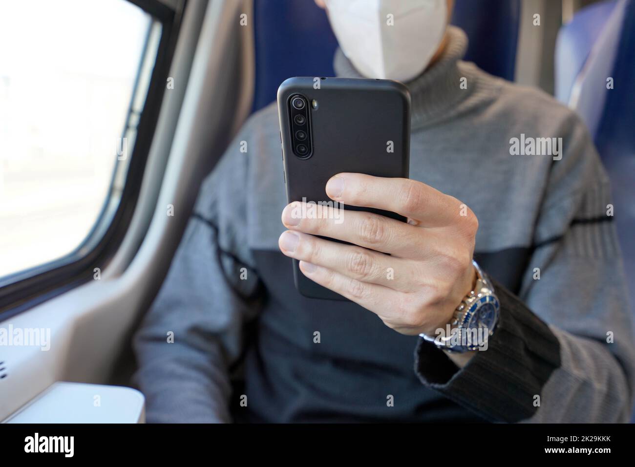 Homme d'affaires dans les transports en commun utilisant une application mobile portant un masque de protection. Train passager tenant un smartphone couvrant le visage avec un masque KN95 FFP2. Concentrez-vous sur le téléphone. Banque D'Images
