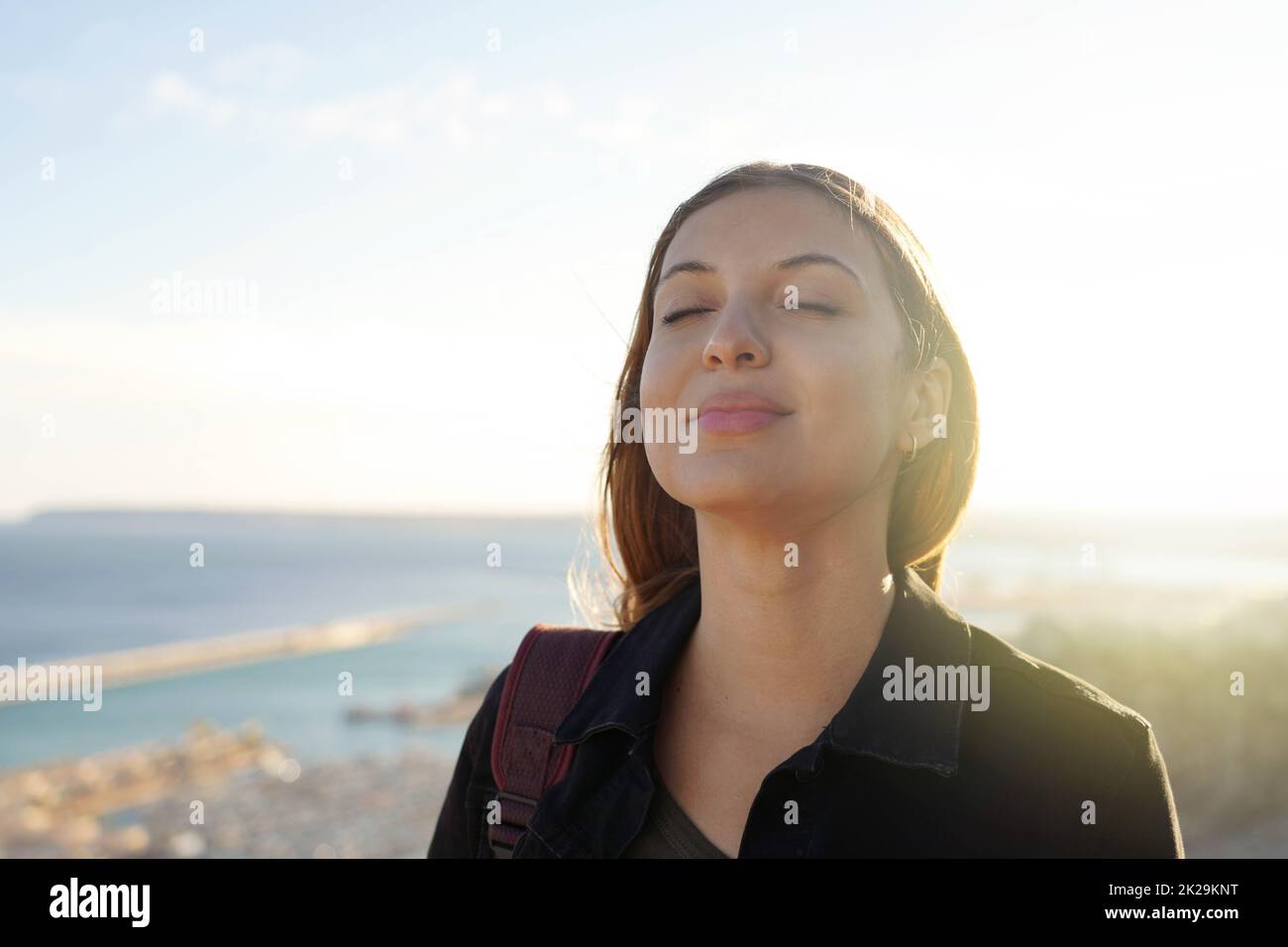 Belle jeune femme avec les yeux fermés respiration relaxante appréciant le soleil au coucher du soleil. Beauté soleil fille portrait. Banque D'Images