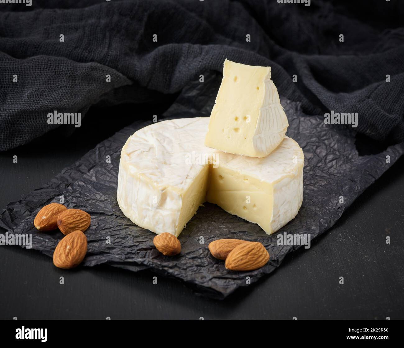 fromage brie rond sur papier froissé noir, table en bois Banque D'Images