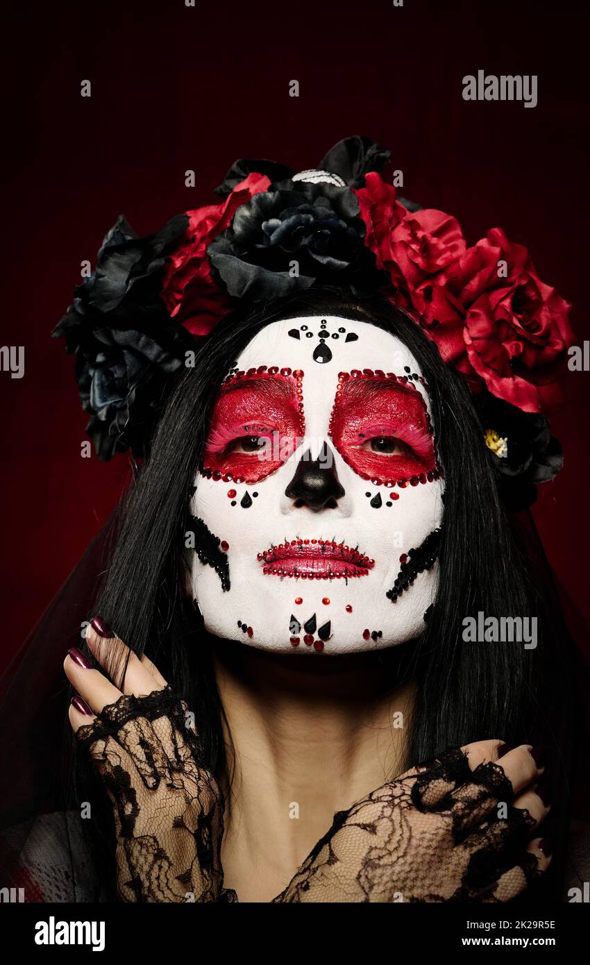 portrait d'une belle femme avec un maquillage de crâne de sucre avec une couronne de fleurs sur sa tête, fond rouge Banque D'Images