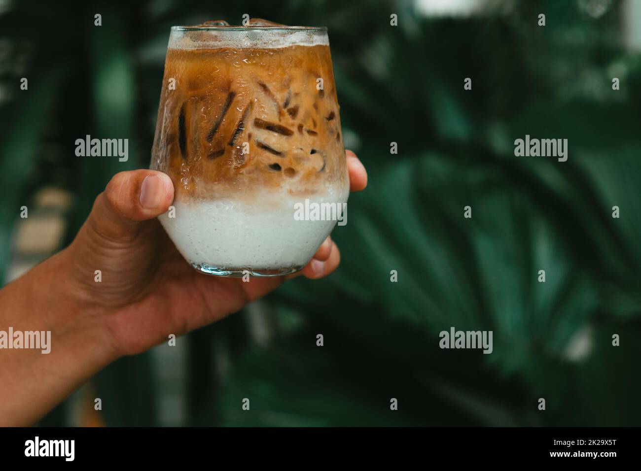 Tenez à la main le café glacé au latte dans un verre avec de la crème sur le fond. Arrière-plan froid de boisson d'été Banque D'Images