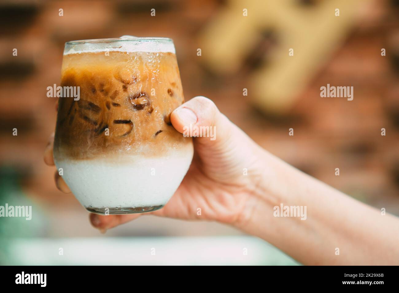 Tenez à la main le café glacé au latte dans un verre avec de la crème sur le fond. Arrière-plan froid de boisson d'été Banque D'Images