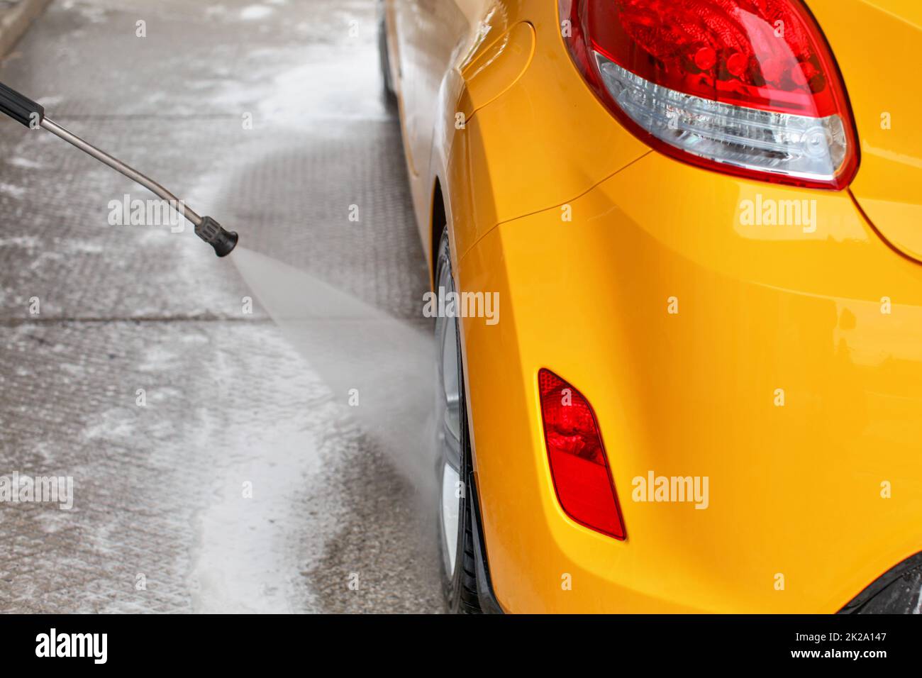 Roue arrière de voiture jaune lavé avec de l'eau jet dans le libre service carwash. Vue de derrière. Banque D'Images