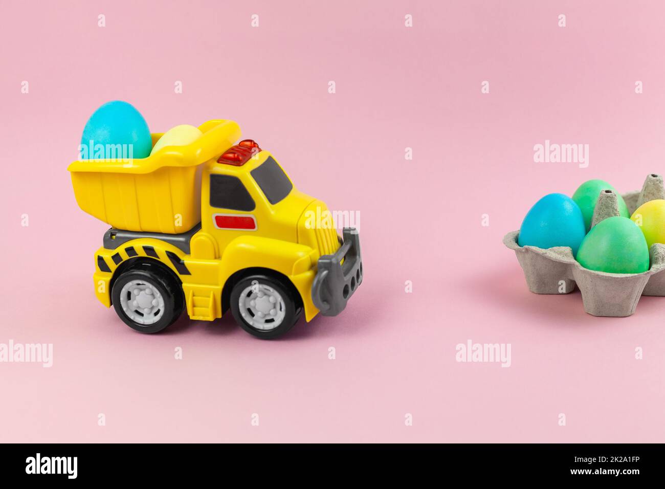 Un camion jaune jouet transportant des œufs de Pâques dans des couleurs pastel. Carte de Pâques avec place pour le texte sur fond rose. Livraison de nourriture de Pâques Banque D'Images