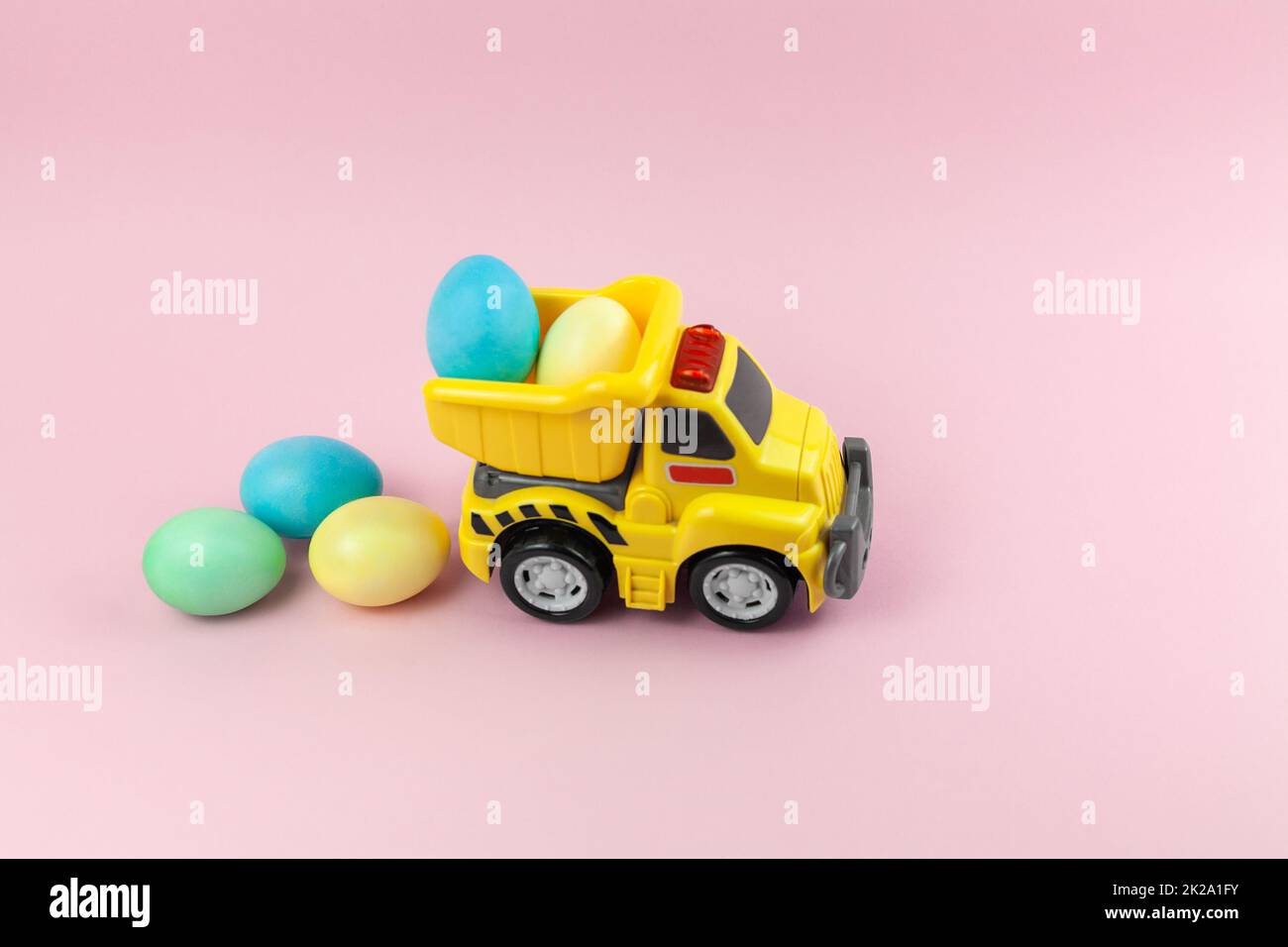 Un camion jaune jouet transportant des œufs de Pâques dans des couleurs pastel. Carte de Pâques avec place pour le texte sur fond rose. Livraison de nourriture de Pâques Banque D'Images