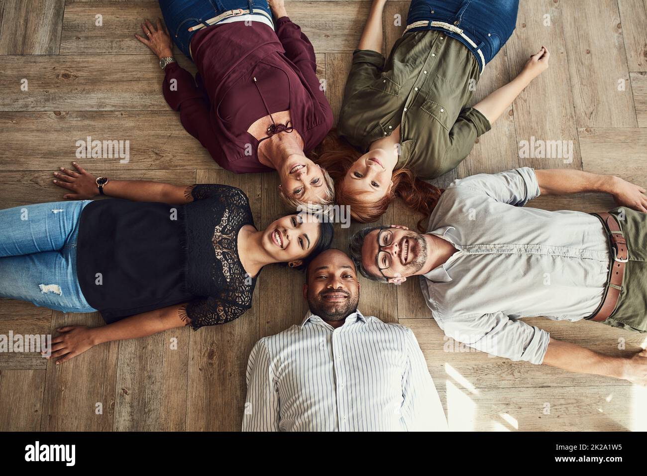 Nous le gardons décontracté mais toujours professionnel. Portrait en grand angle d'un groupe de collègues se trouvant ensemble dans un cercle sur le sol au travail. Banque D'Images