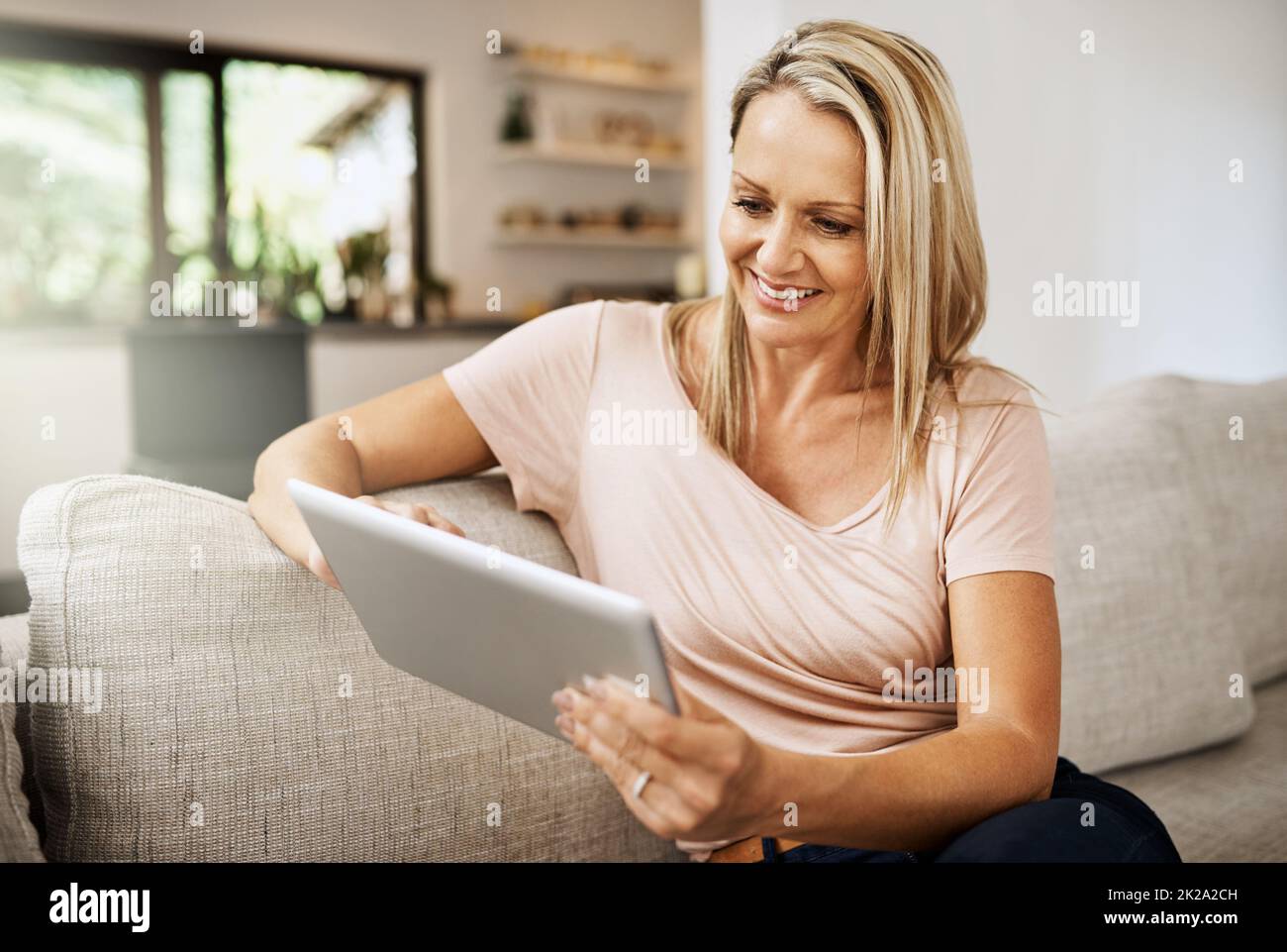 Messagerie instantanée sociale même lorsque vous êtes seul à la maison. Photo d'une femme mûre utilisant sa tablette numérique tout en se relaxant sur son canapé à la maison. Banque D'Images