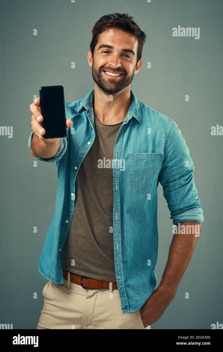 Jetez un œil et dites-moi ce que vous pensez. Portrait studio d'un beau jeune homme tenant un téléphone portable avec un écran vierge sur fond gris. Banque D'Images