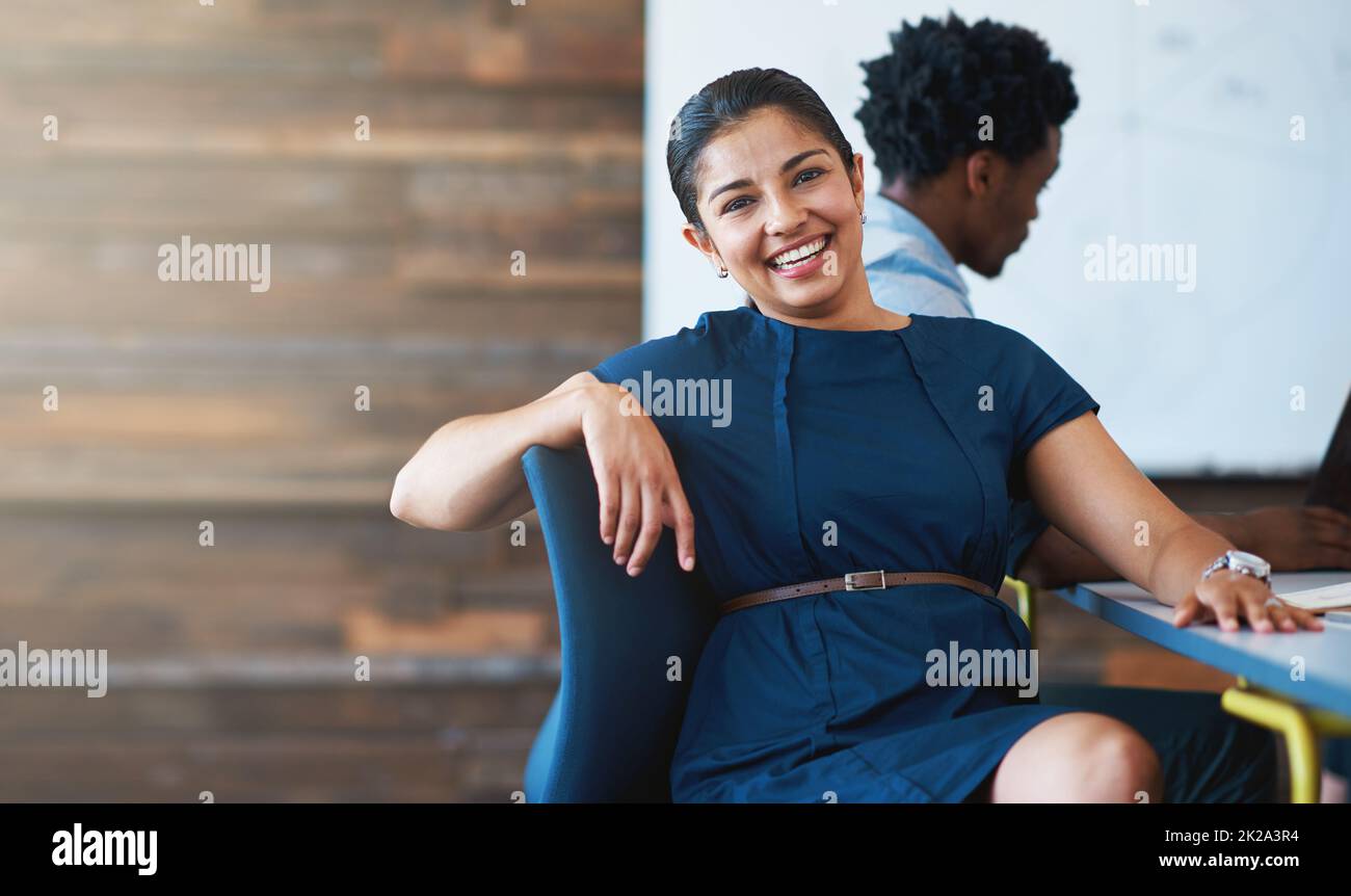 Avoir une excellente journée au travail. Une jeune femme d'affaires assise dans une chaise de bureau avec un collègue en arrière-plan. Banque D'Images