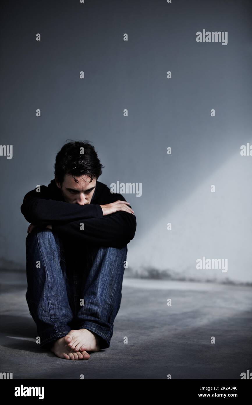Gérer le stress émotionnel. Un jeune homme qui a l'air inquiet en étant assis pieds nus sur le sol. Banque D'Images