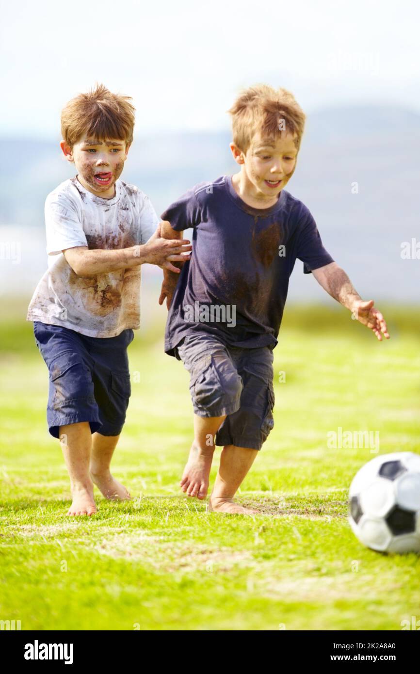 Avoir un jeu amical. Deux petits garçons adorables jouant au football ensemble à l'extérieur tout en étant couverts de boue. Banque D'Images