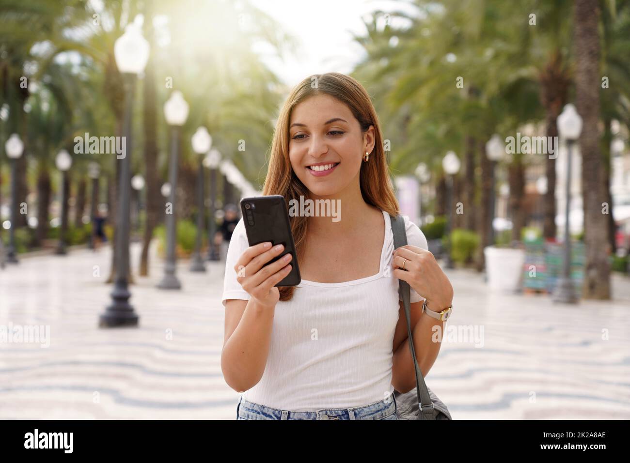 Une jeune femme souriante de taille moyenne utilise un smartphone pour lire les actualités des réseaux sociaux recherche texte envoie des e-mails en ligne dans la rue. La technologie des personnes. Banque D'Images