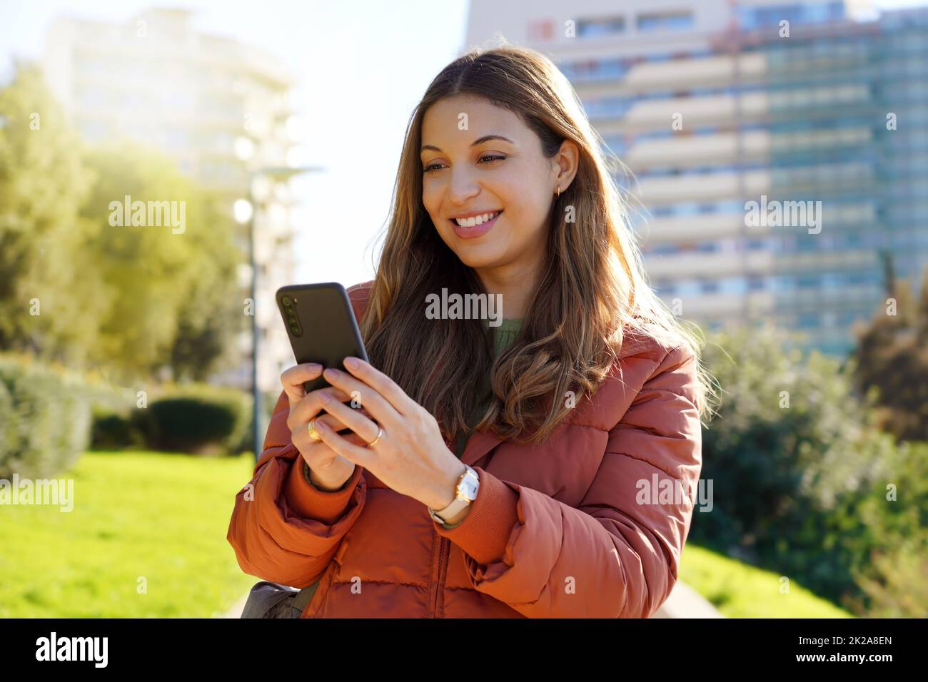 Portrait d'une fille à l'extérieur en utilisant un smartphone portant un manteau d'hiver regardant la vidéo en streaming Banque D'Images
