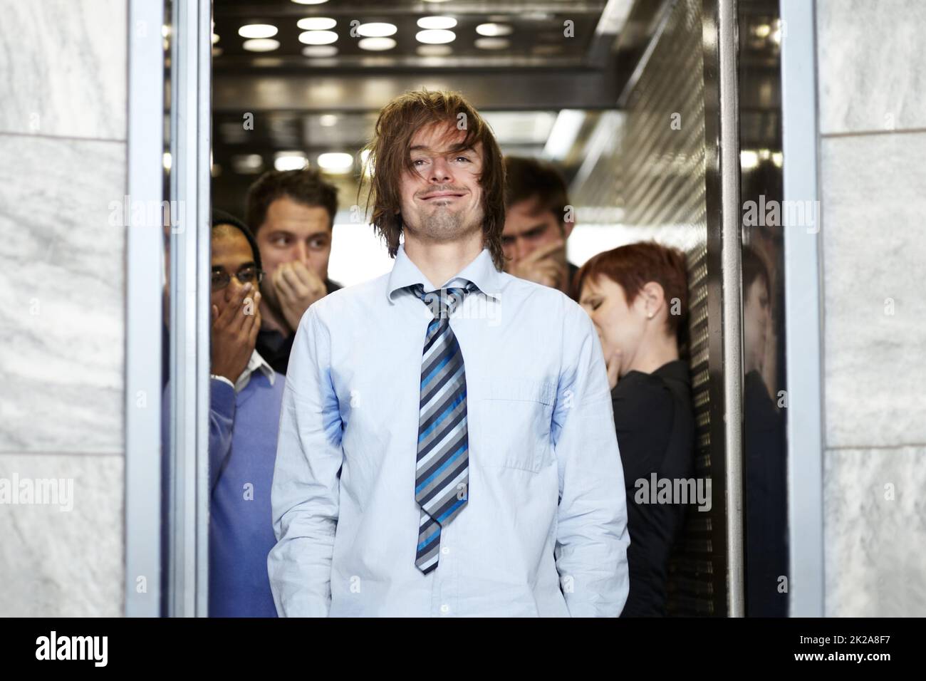 Il a besoin d'une douche. Un jeune homme d'affaires sale affectant ses collègues dans un ascenseur. Banque D'Images