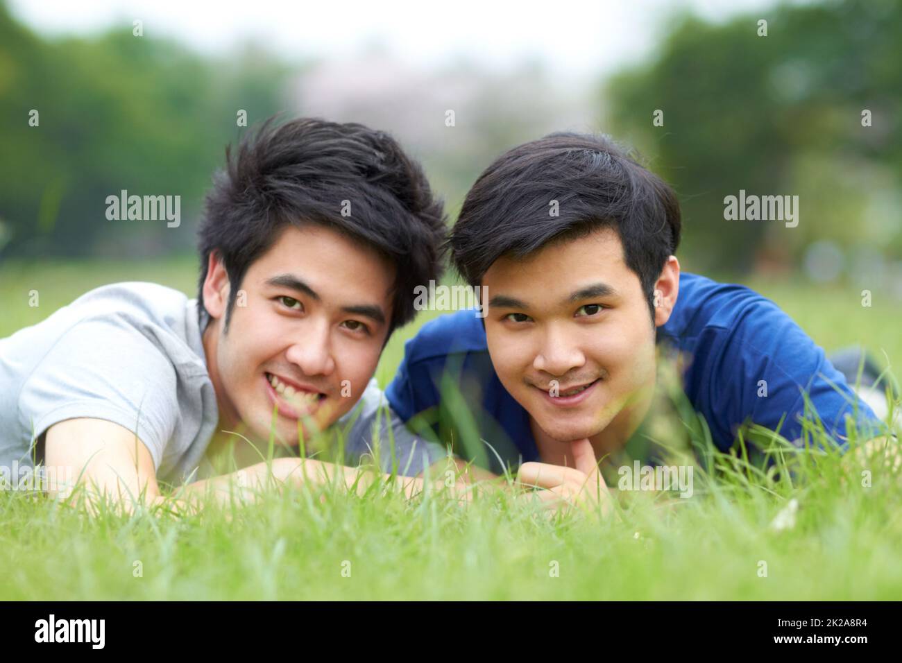 Ils partagent un amour du plein air. Mignon jeune couple asiatique gay souriant ensemble tout en étant allongé sur l'herbe. Banque D'Images