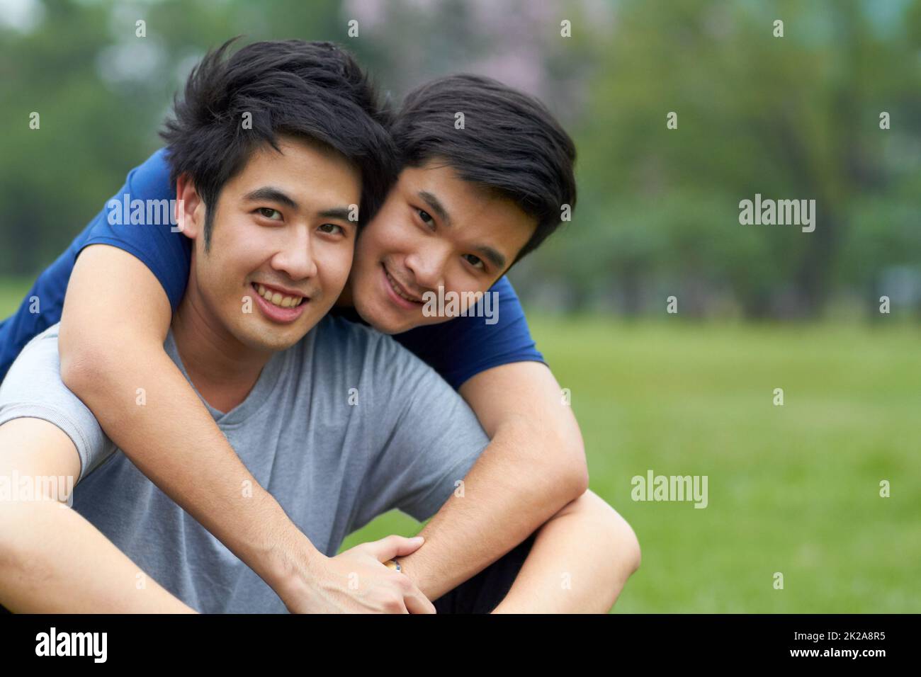 Vivre et aimer ensemble. Mignon jeune gay asiatique couple souriant ensemble tout en étant assis dans le parc. Banque D'Images