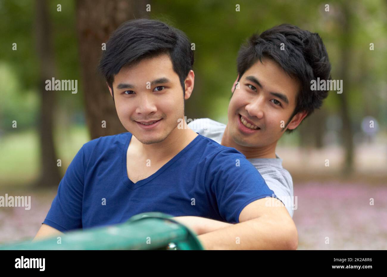 Profiter de la liberté d'être eux-mêmes. Mignon jeune gay asiatique couple souriant ensemble tout en étant assis dans le parc. Banque D'Images