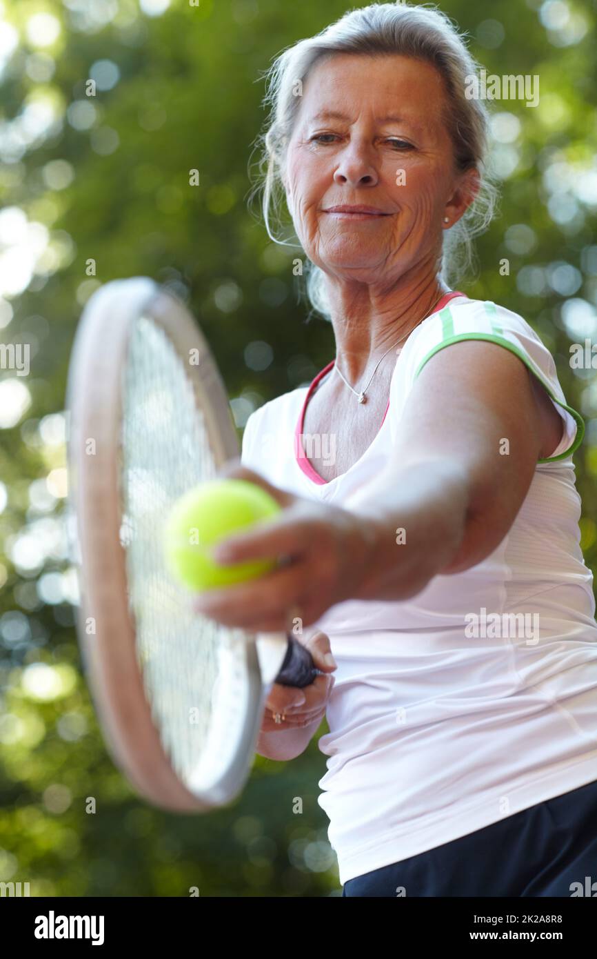 En gardant l'œil sur le ballon. Femme âgée se prépare à servir - tennis. Banque D'Images