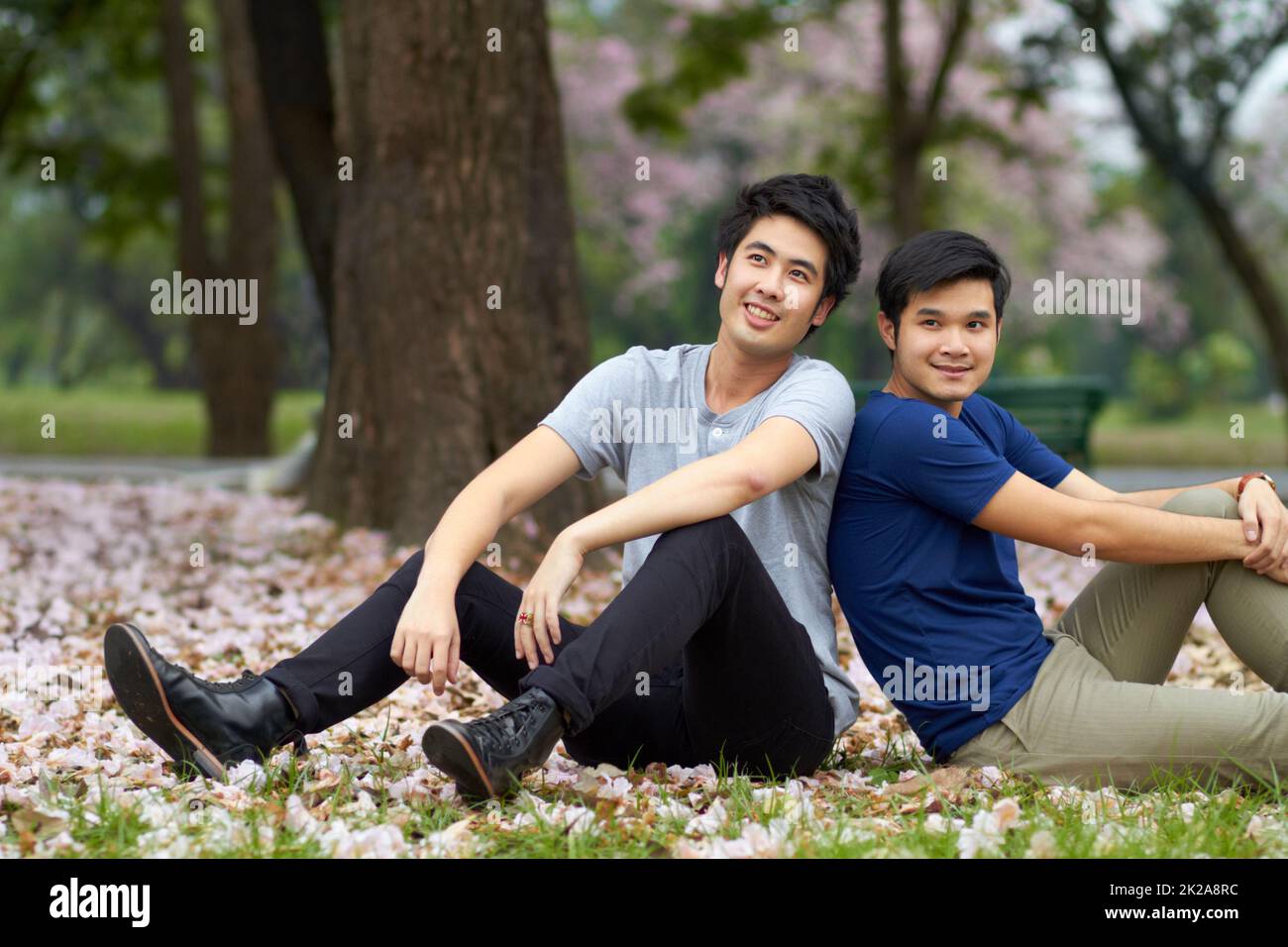 C'est toujours là pour les uns les autres. Mignon jeune gay asiatique couple souriant ensemble tout en étant assis dans le parc. Banque D'Images