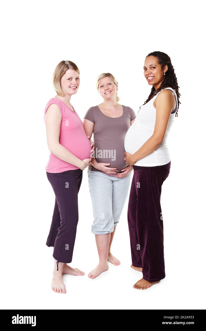 Je me sens déjà protecteur. Trois femmes enceintes souriant largement à la caméra tout en se tenant debout contre un fond blanc tenant leurs estomacs. Banque D'Images