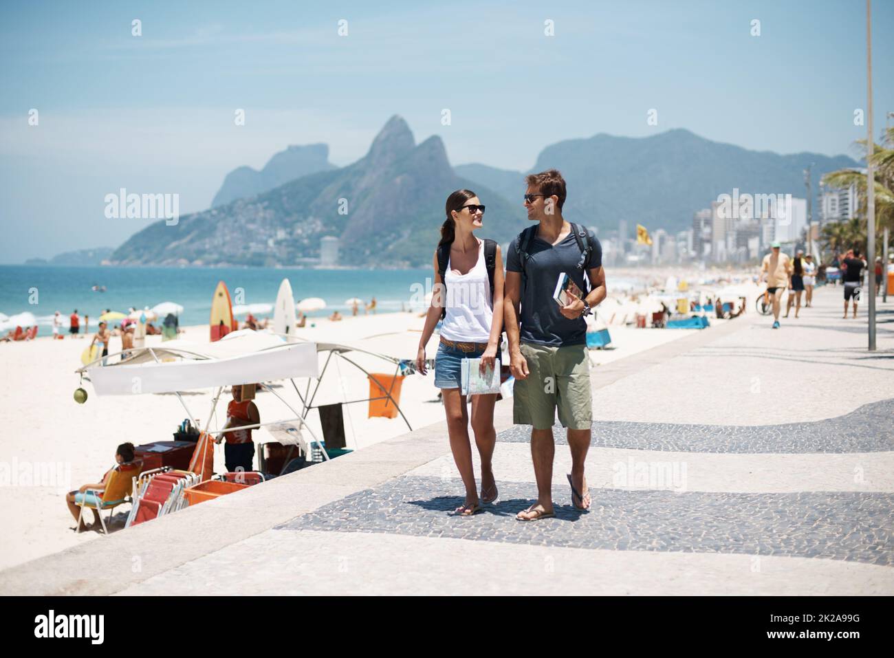 Profiter de la plage avec un freind. Photo courte d'un jeune couple qui marche le long d'une plage animée. Banque D'Images