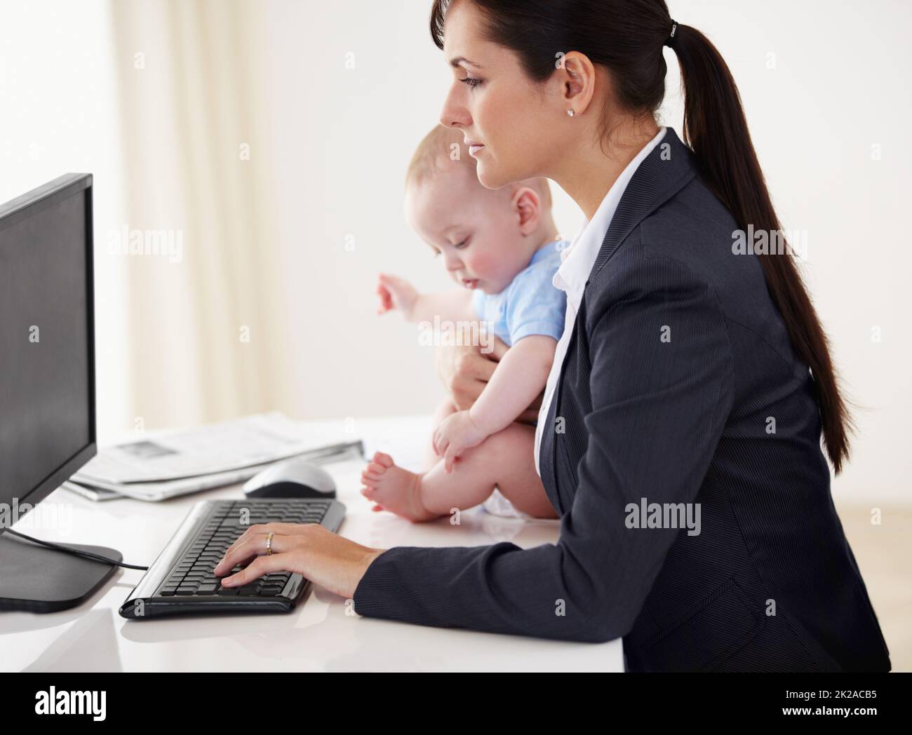 Mummys a eu un travail à faire Une jeune mère qui travaille tient un bébé tout en travaillant sur son ordinateur. Banque D'Images