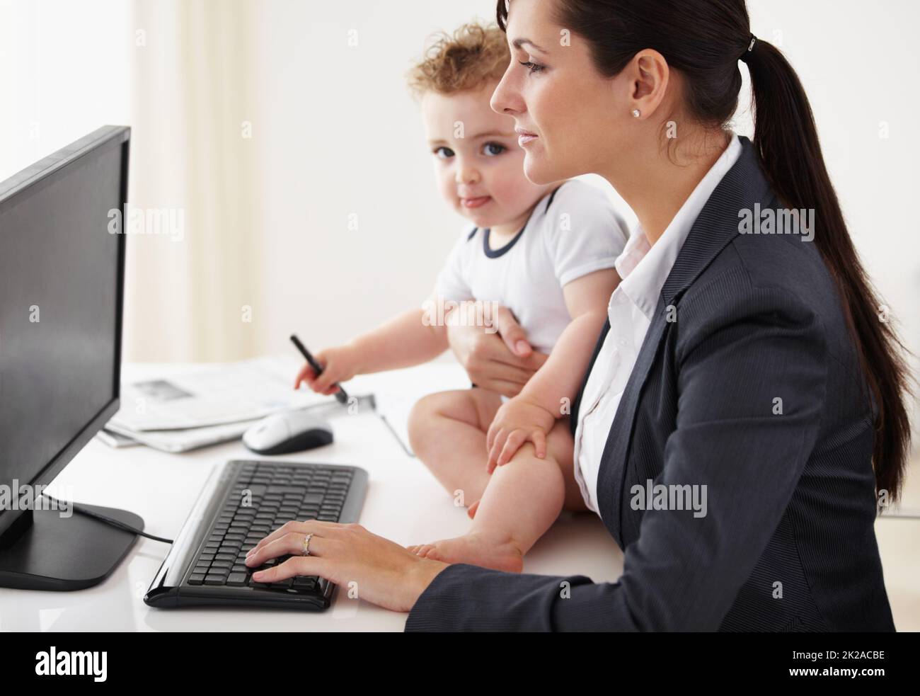 Être une maman qui travaille prend de super pouvoirs. Mère travaillant tenant un bébé tout en travaillant sur son ordinateur. Banque D'Images