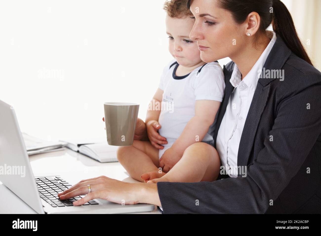 Maman qui travaille. Jeune mère qui travaille tient un bébé tout en travaillant et en buvant du café. Banque D'Images